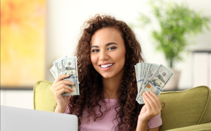 woman at her laptop holding hundred dollar bills